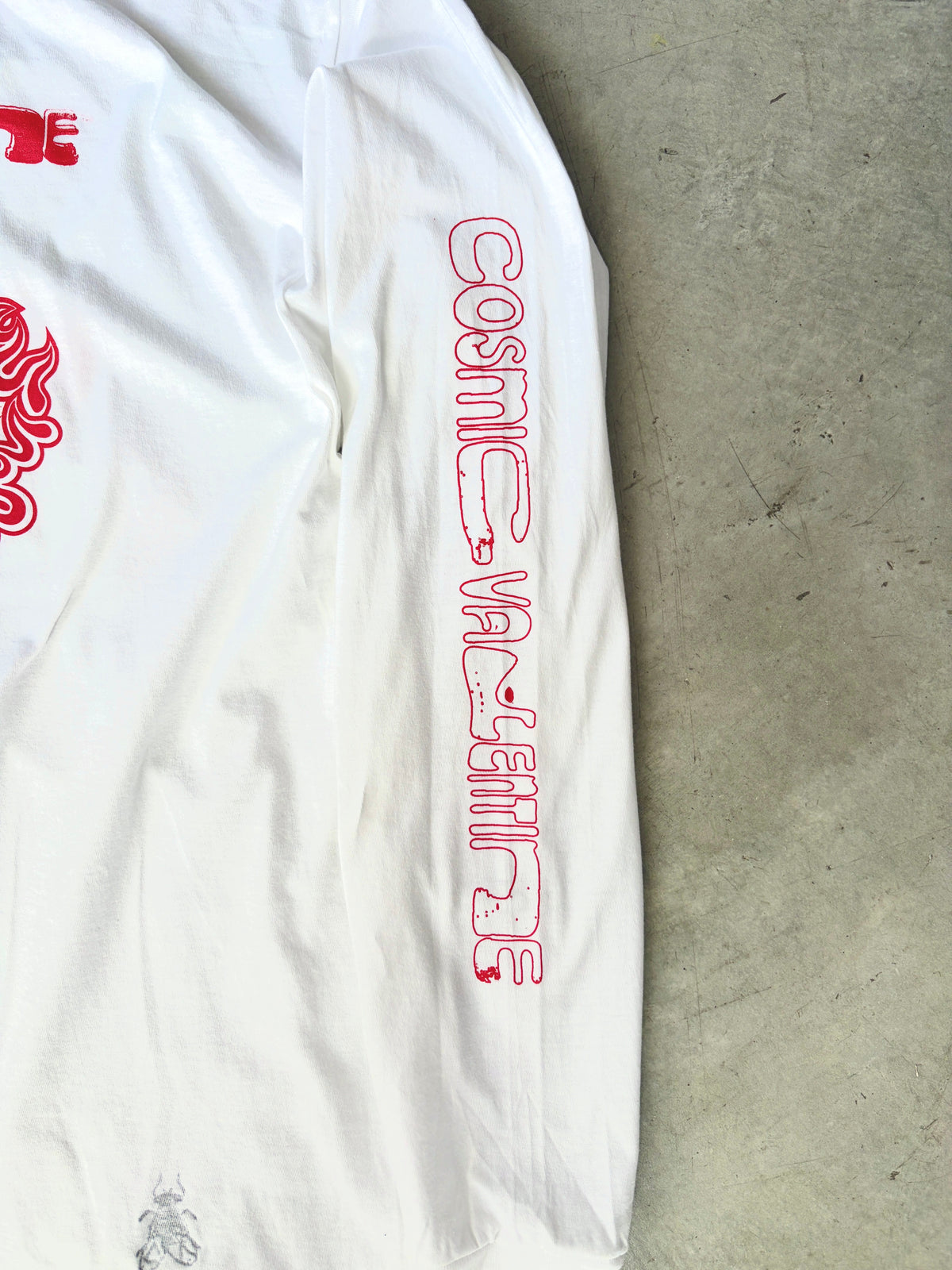 Close-up of a sleeve with red outlined Cosmic Valentine text and a small black beetle graphic near the hem