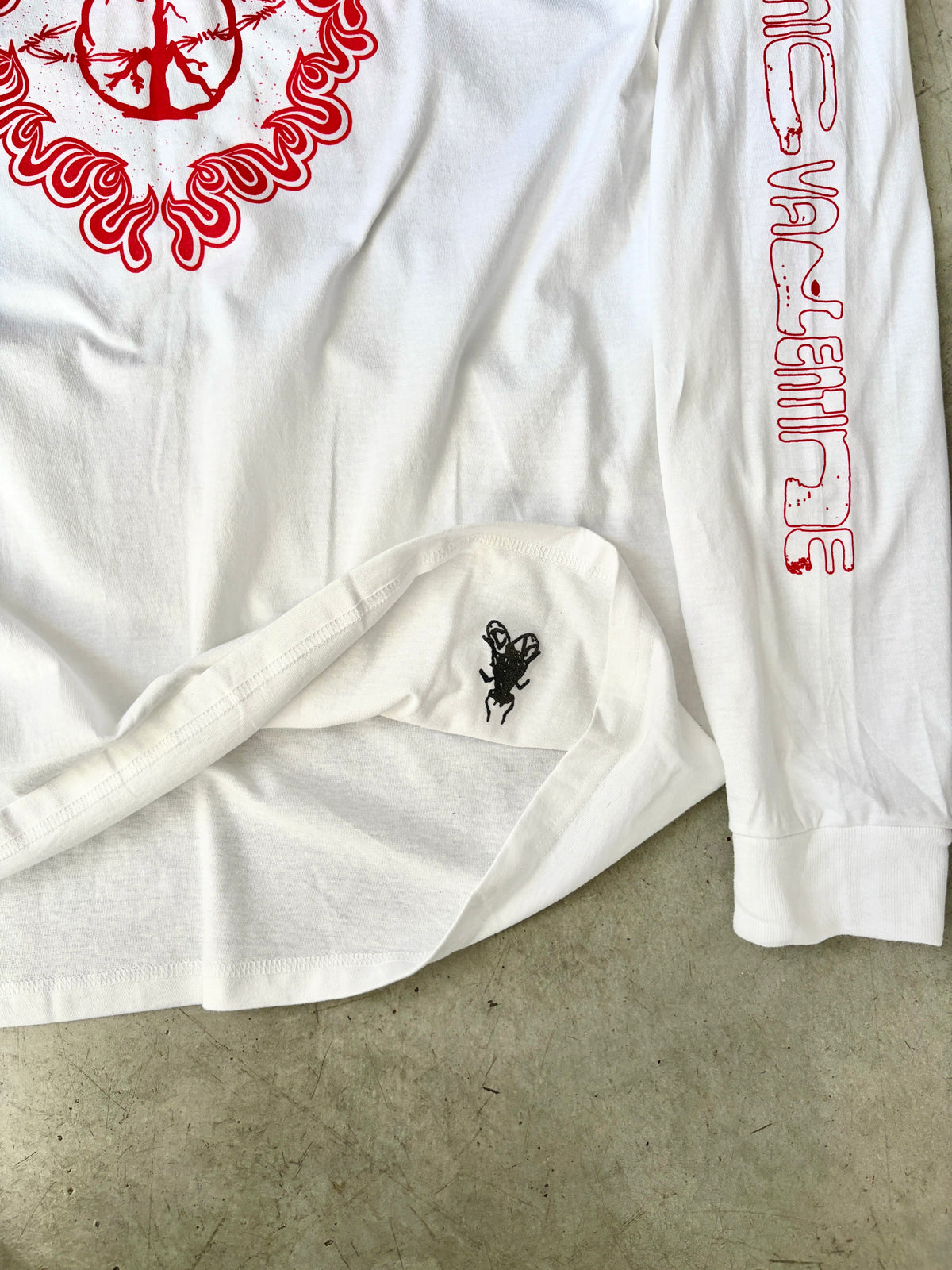 Close-up of the shirt hem showing a small black beetle print and red Cosmic Valentine sleeve text