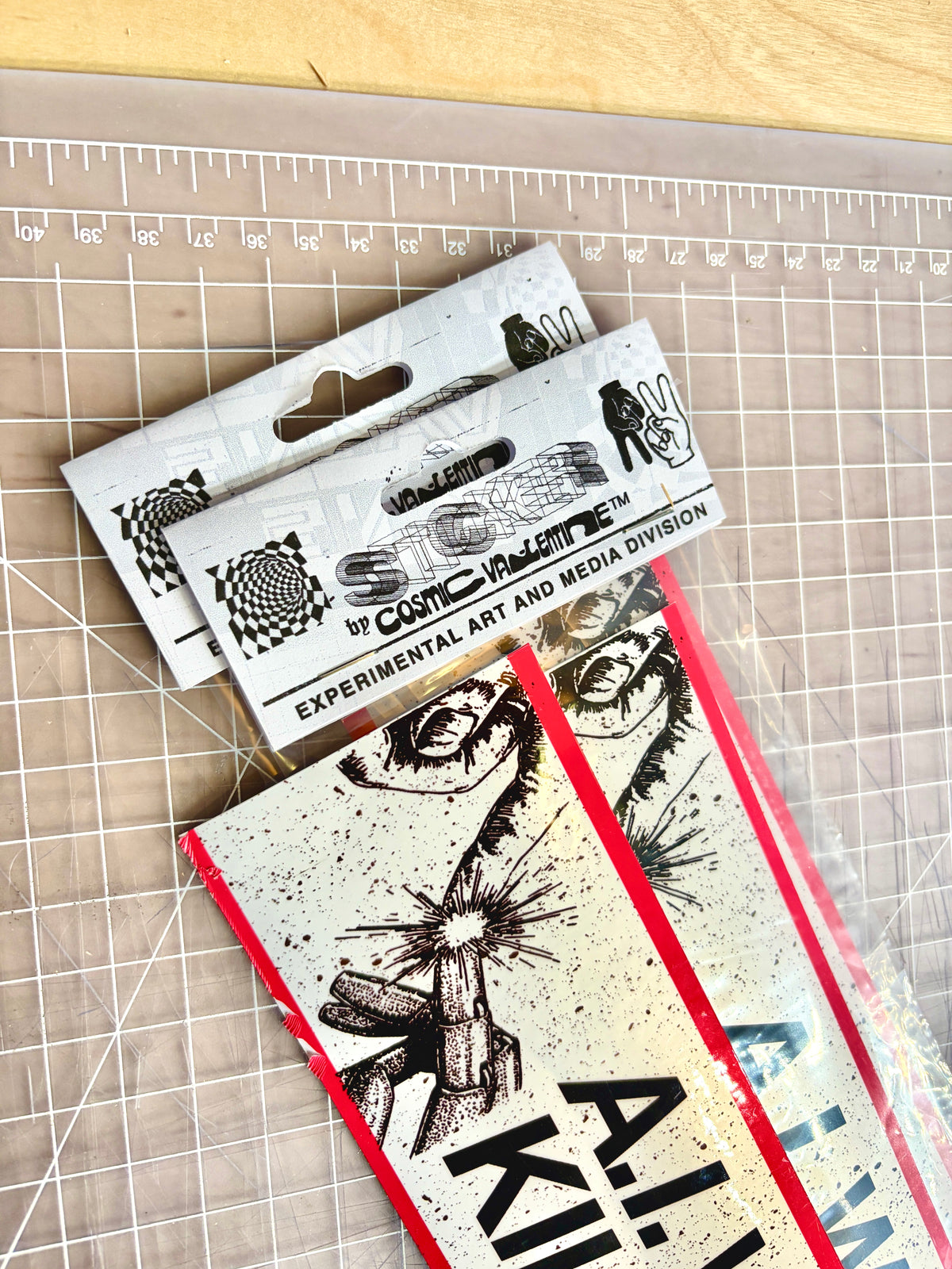 Packaged vinyl stickers with header cards reading Sticker by Cosmic Valentine, on a cutting mat
