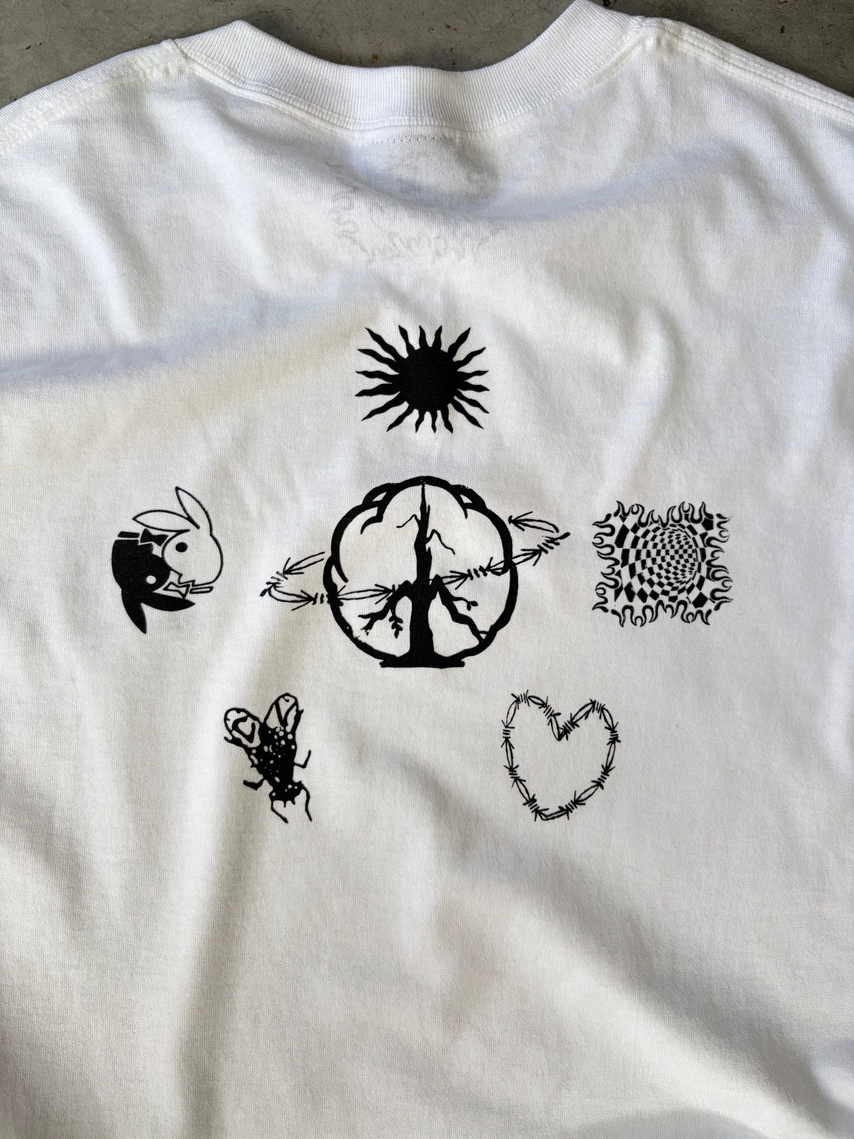 White t-shirt with black abstract designs including a sun, brain, rabbit, fly, heart, and intricate pattern on the back.