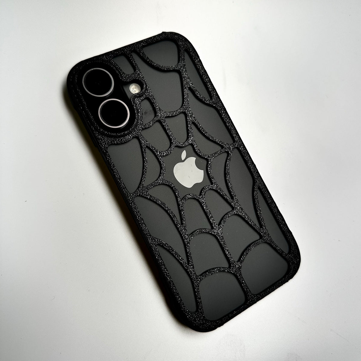 Black spiderweb snap case on an iPhone, back view with the Apple logo showing through the web
