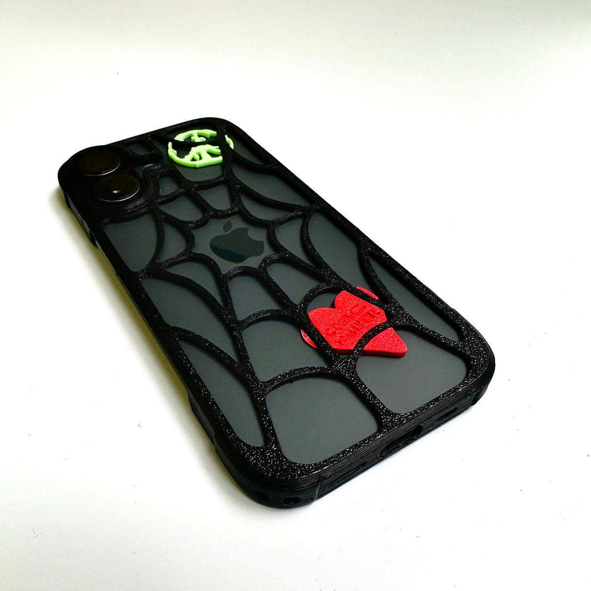 Black spiderweb iPhone case with a red heart and green peace piece, angled view
