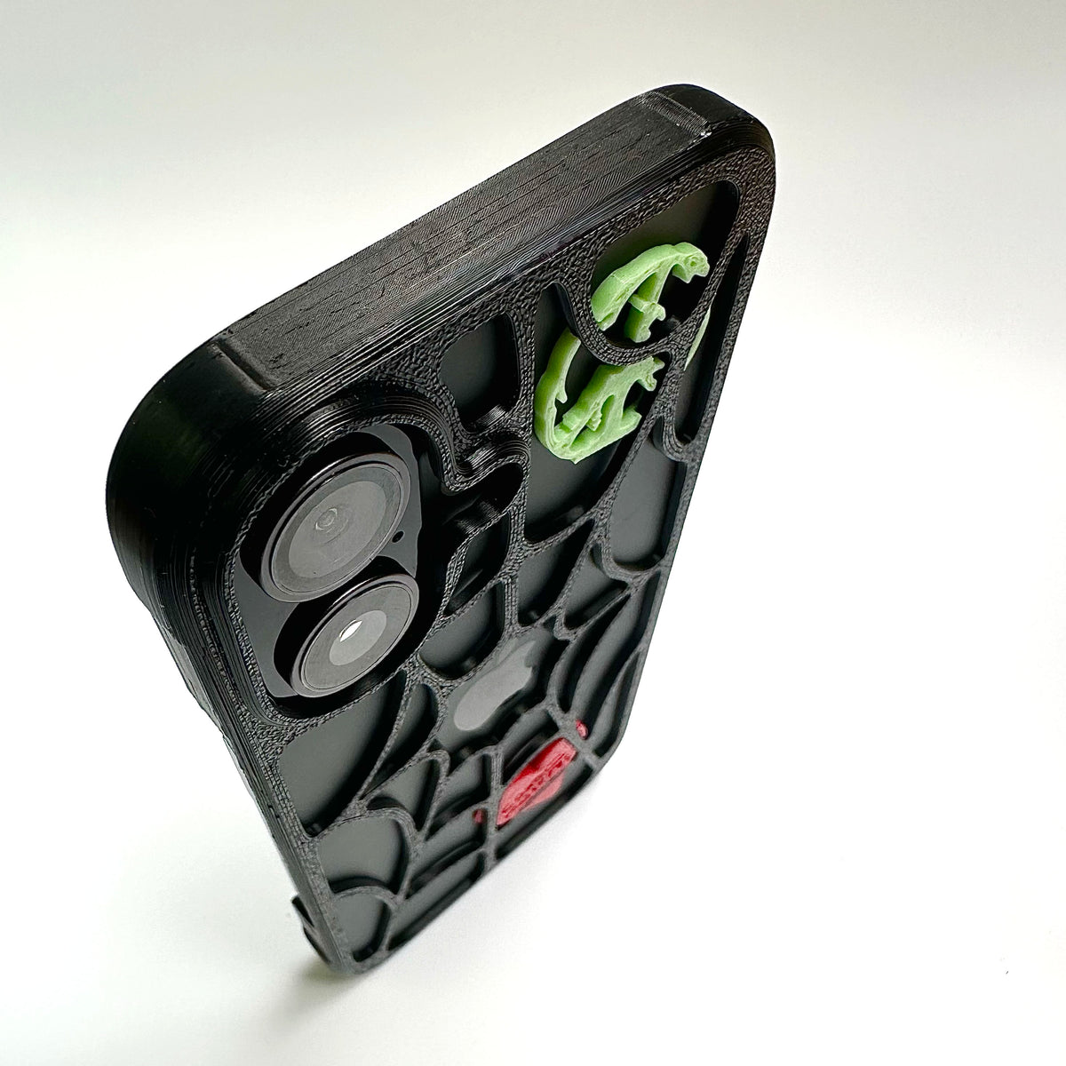 Black spiderweb iPhone case with a green peace piece and red heart, close-up of the camera cutout