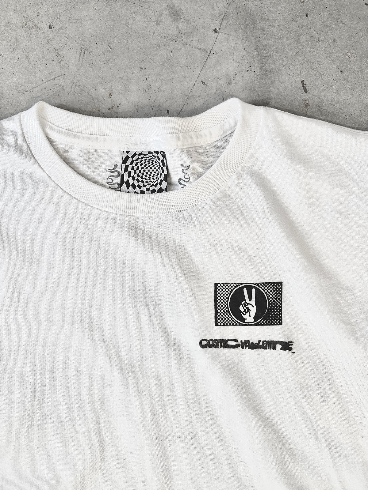 White t-shirt with a black graphic of a hand showing a peace sign and the text "COSMIC VALENTINE" below it.