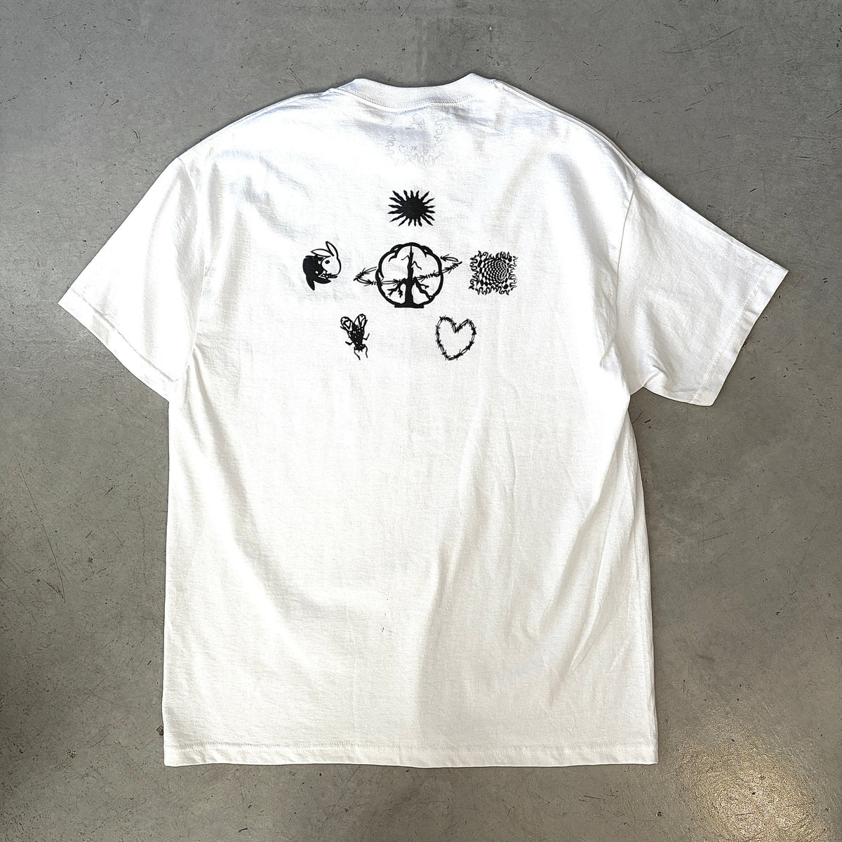 White short-sleeve t-shirt with black graphic designs, including a sun, heart, and abstract shapes, on the back.
