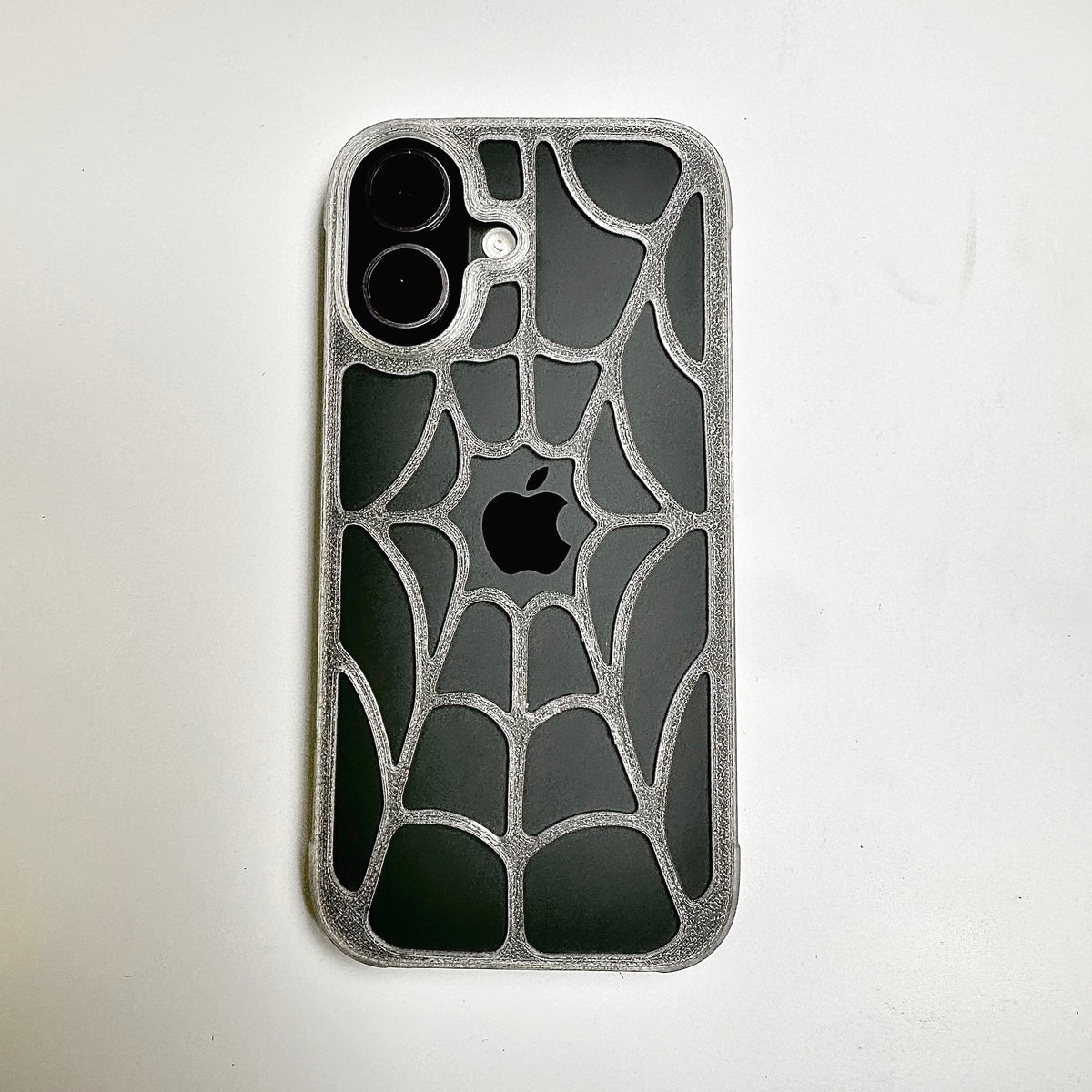 Clear-edged spiderweb snap case on an iPhone, back view showing the web pattern and camera opening