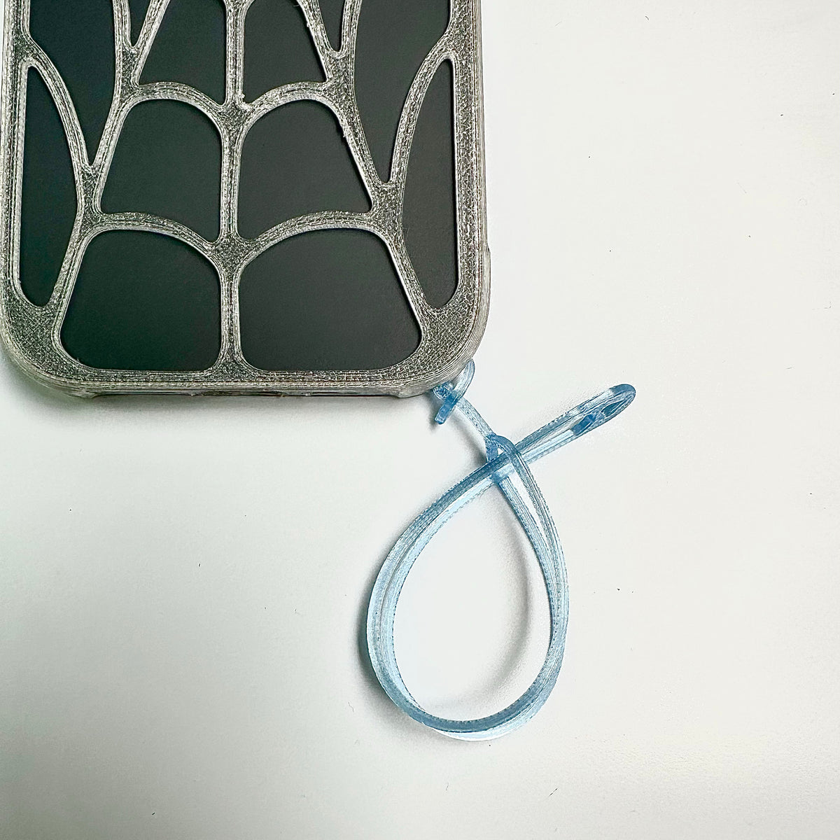 Corner of a clear spiderweb iPhone case with a blue wrist tether attached